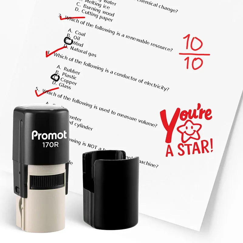 Black self inking stamp and removable cap displayed beside a graded science worksheet marked with red check marks, a “10/10” score, and a smiling star stamp that says “You’re A STAR!” The worksheet includes multiple choice science questions, and this ink