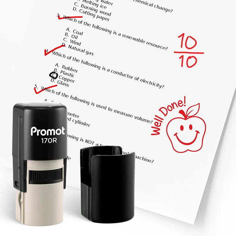 Black self inking teacher stamp and removable cap displayed beside a graded science worksheet marked with red check marks and a “10/10” score. A red apple stamp on the page says “Well Done!” showing how the classroom stamp can be used to reward student ac