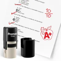 Black self inking teacher stamp and removable cap displayed beside a graded science worksheet marked with red check marks and a “10/10” score. A red apple stamp with a worm and “A+” design appears on the page, showing how the classroom stamp can reward ex