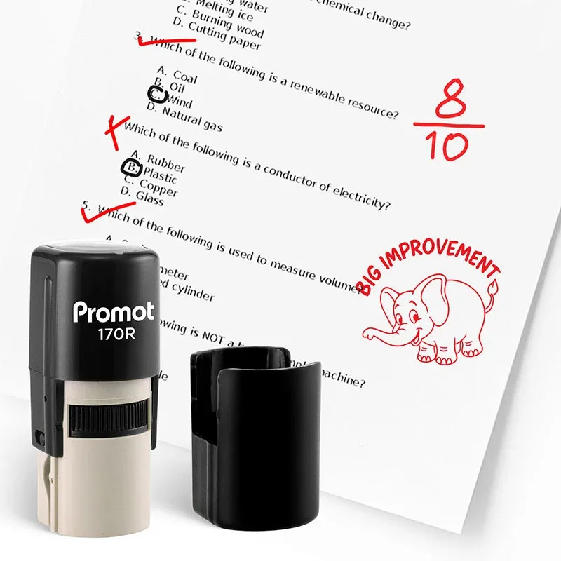 Black self inking teacher stamp and removable cap displayed beside a graded worksheet marked with red check marks and an “8/10” score. A red elephant stamp with the text “BIG IMPROVEMENT” is stamped on the paper, showing encouraging classroom feedback for
