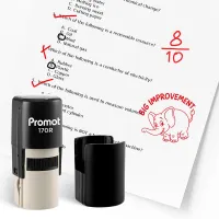 Black self inking teacher stamp and removable cap displayed beside a graded worksheet marked with red check marks and an “8/10” score. A red elephant stamp with the text “BIG IMPROVEMENT” is stamped on the paper, showing encouraging classroom feedback for