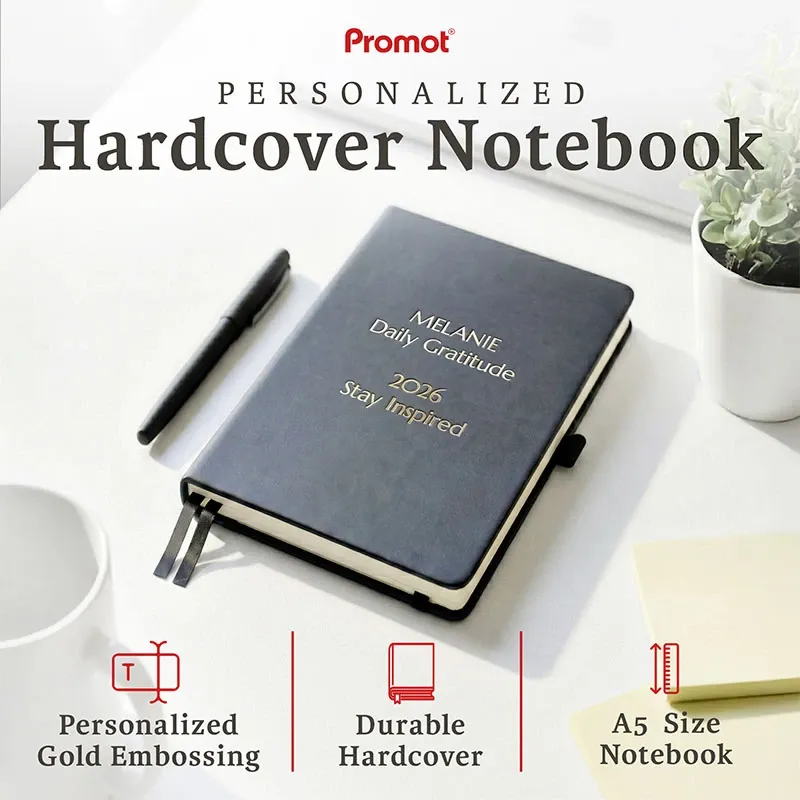 Black hardcover personalized leather journal with custom gold embossed text, displayed on a desk with a pen and plant.