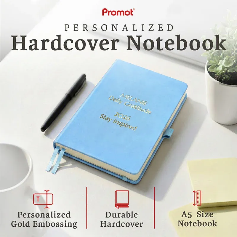 Sky blue notebook with custom gold embossing on a desk beside a pen, a personalized leather journal with a durable hardcover.