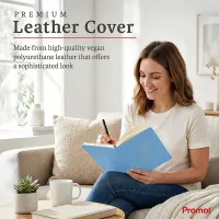 Person writing in a blue notebook while relaxing on a sofa, a personalized leather journal with a premium vegan leather cover.