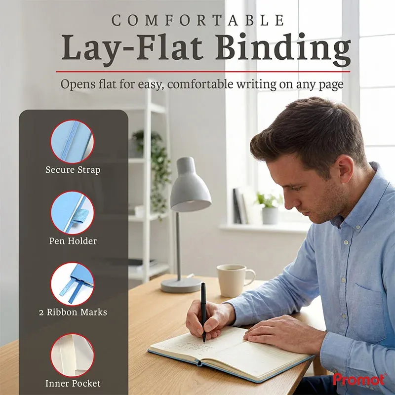 Person writing in an open notebook at a desk, a personalized leather journal with lay-flat binding, pen holder, and ribbon bookmarks.
