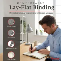 Man writing in an open notebook at a desk, a personalized leather journal with lay-flat binding and built-in accessories.