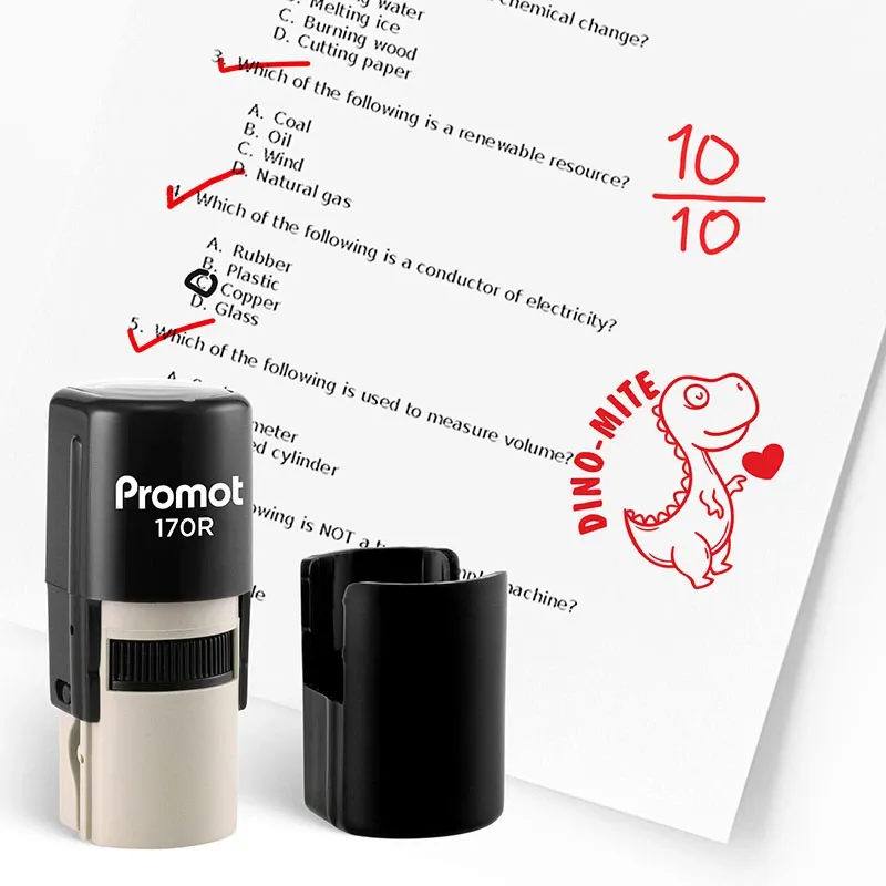 Black self inking teacher stamps for grading displayed beside a marked worksheet with red checkmarks and a “10/10” score. A red dinosaur stamp with the text “DINO-MITE” is printed on the paper to show fun classroom feedback.