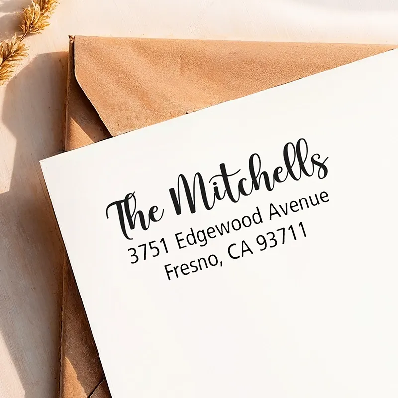 self-inking address stamp impression printed neatly on a white envelope resting over a kraft envelope with a custom return address.