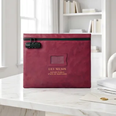 Notary bag with lock in burgundy red, personalized with a gold foil name, on a white marble desk