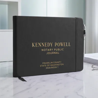 Black personalized notary journal with gold foil custom text, elastic strap, and pen holder on a marble desk