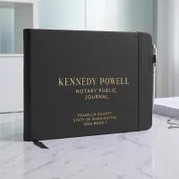 Black personalized notary journal with gold foil custom text, elastic strap, and pen holder on a marble desk